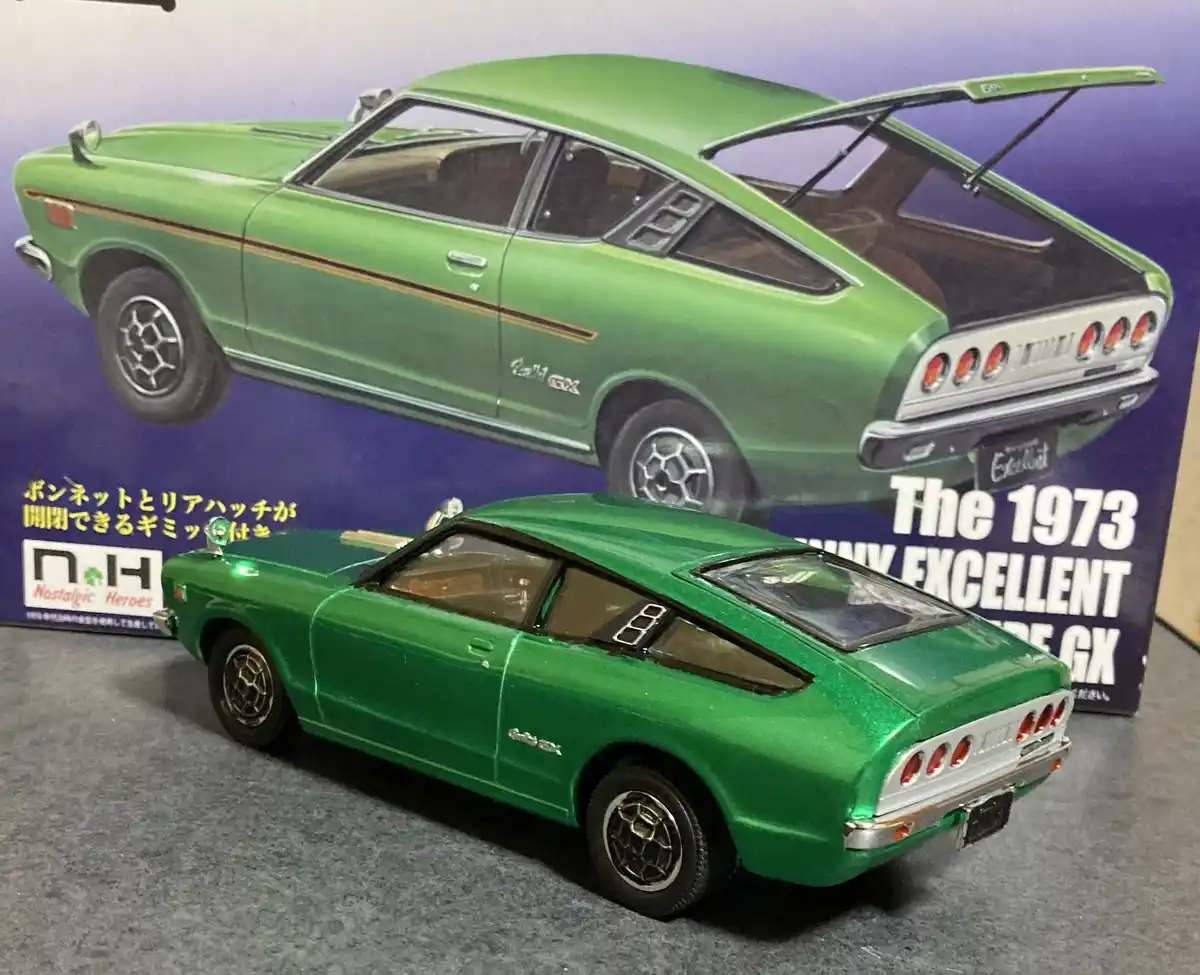 A green die-cast model of a 1973 Toyota Celica GX is shown in front of its packaging, which features an identical car image…