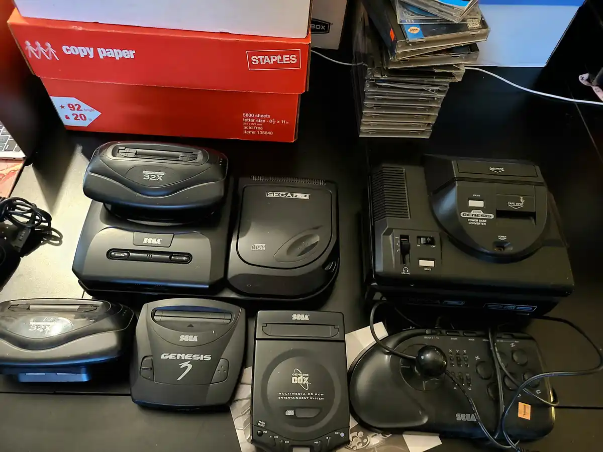 A collection of Sega Genesis gaming hardware, including multiple 32X add-ons, Genesis CD-ROM units, a Power Base Converter…