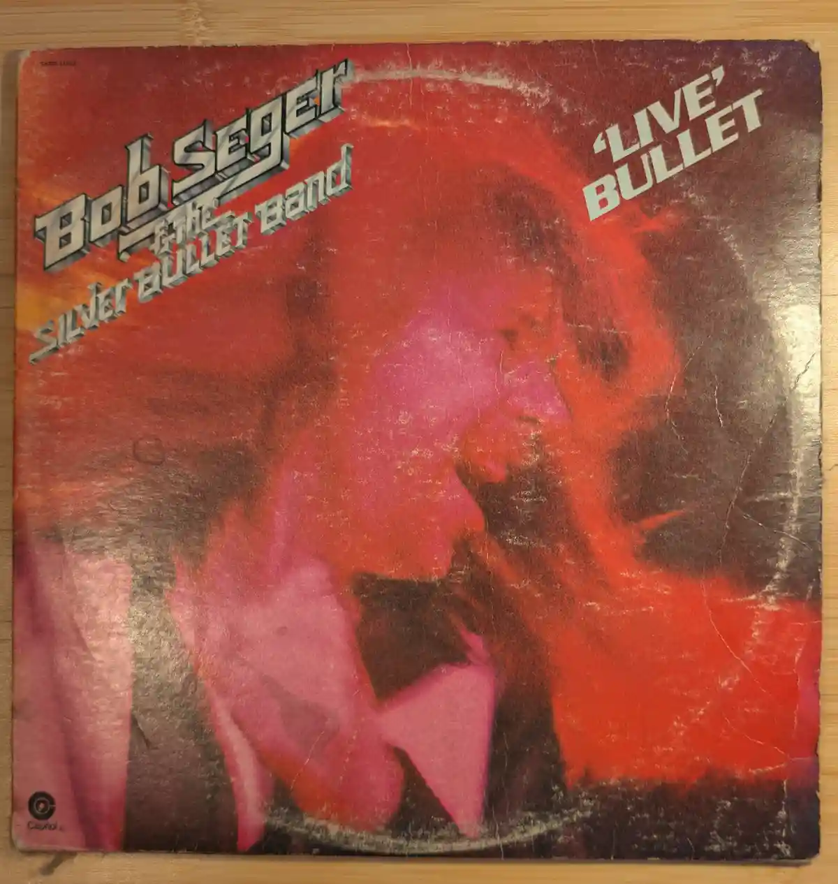 A weathered, red-toned album cover for Bob Seger and the Silver Bullet Band's 'Live' Bullet, showing a stylized, close-up…