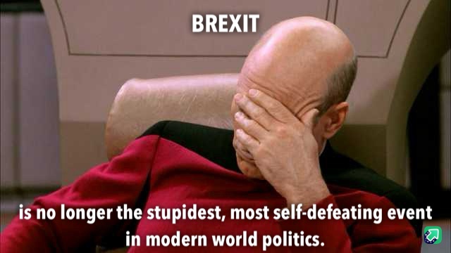 A bald man in a red uniform sits in a chair, covering his face with his hand in a gesture of despair or exasperation. The…