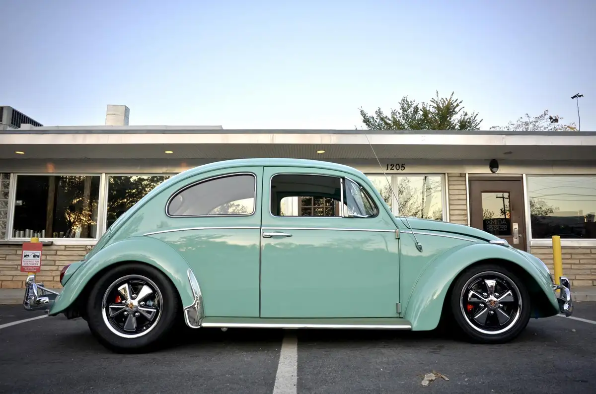 a mint green classic volkswagen beetle with custom black wheels and chrome trim is parked in a parking lot in front of a…
