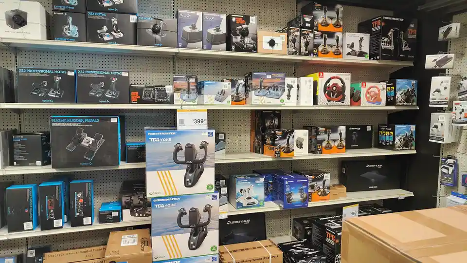 A retail store aisle filled with boxes of flight simulation hardware, including yokes, HOTAS systems, and rudder pedals from…
