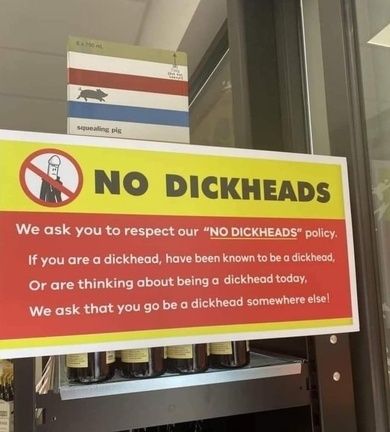 A bright yellow and red sign in a store displays a 'NO DICKHEADS' policy with a crossed-out person icon. The text humorously…