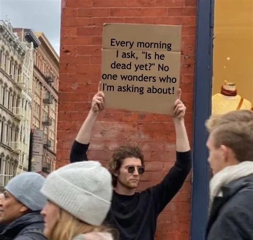 A man with curly hair and sunglasses holds up a cardboard sign with text on it while standing on a city street. Several…