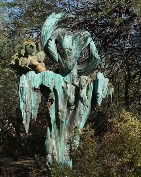 A weathered, verdigris-covered bronze sculpture of a stylized cactus with a large, curved horn-like structure on top…