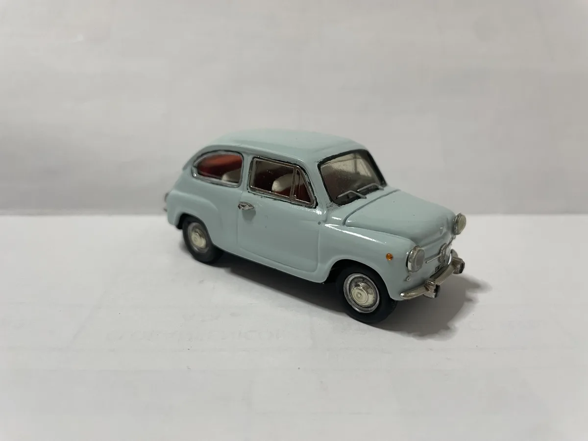 A light blue vintage toy car, resembling a Fiat 500, is photographed against a plain white background. The car has red…