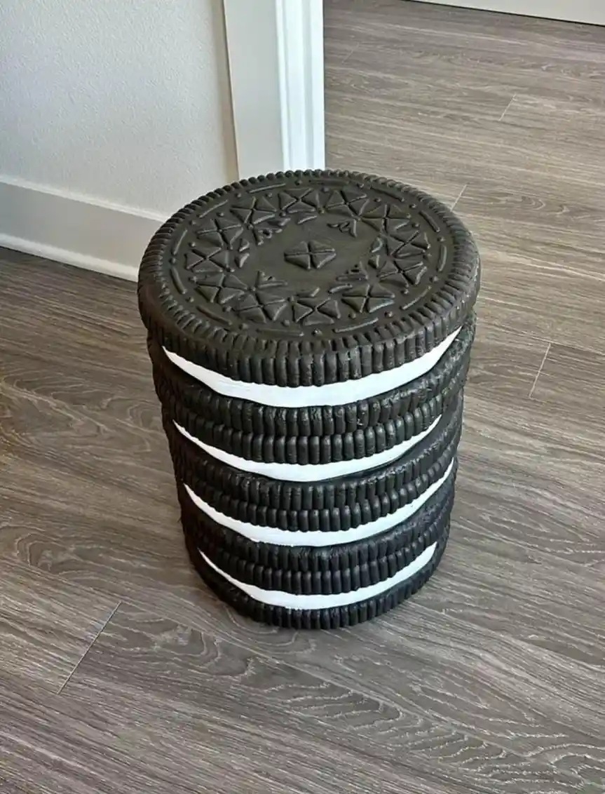 a tall, cylindrical stool made to look like a stack of four Oreo cookies, sitting on a wood-laminate floor next to a white…