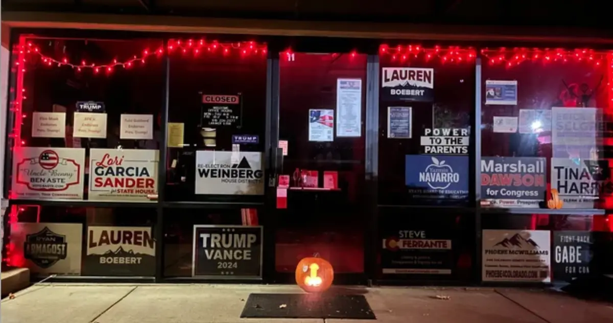 A storefront window at night is covered in numerous political campaign signs for various candidates, including Trump, Lauren…