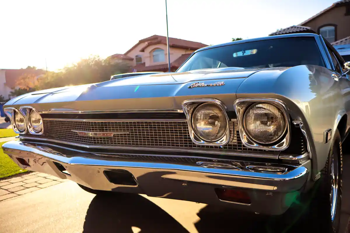 A close-up photo of a shiny, light blue classic American muscle car, likely a Chevrolet Chevelle, parked in a driveway with…