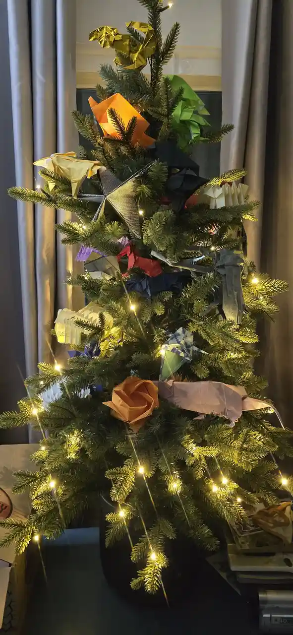 A decorated artificial Christmas tree adorned with numerous colorful origami figures, including animals and flowers…