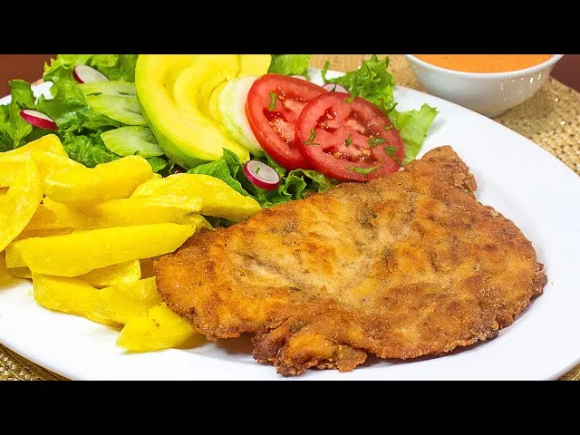 a close-up photo of a golden-brown breaded cutlet, likely chicken or pork, served on a white plate with yellow french fries…