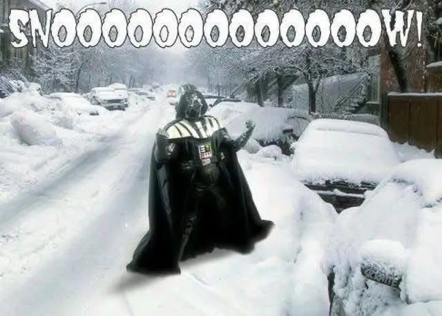 A person dressed as Darth Vader stands in the middle of a snow-covered residential street, surrounded by snow-laden cars and…