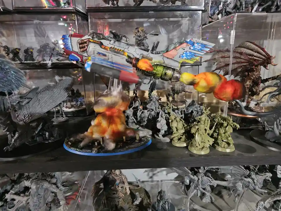 A shelf of painted miniature wargaming figures, including a large spaceship model firing a colorful, fluffy projectile at a…
