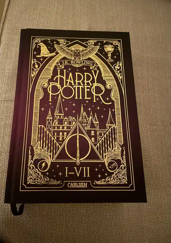 A dark purple hardcover book with gold foil detailing shows the title 'HARRY POTTER' and 'I-VII' beneath a depiction of…
