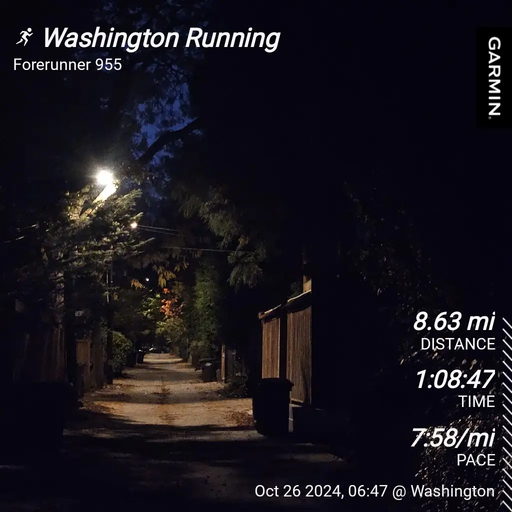 A dark, tree-lined alleyway at night, illuminated by a single streetlamp, overlaid with a Garmin Forerunner 955 running…