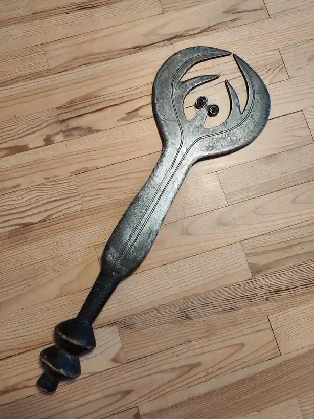 A large, ornate wrench with a decorative, stylized head featuring two small black spiral eyes and a curved mouth, lying…