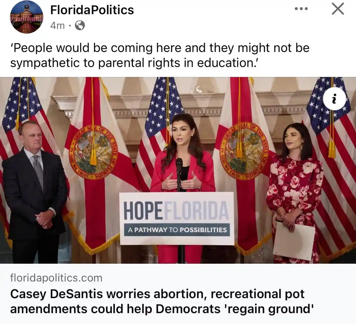 A woman in a pink suit stands at a podium with 'HOPEFLORIDA A PATHWAY TO POSSIBILITIES' written on it, flanked by two other…
