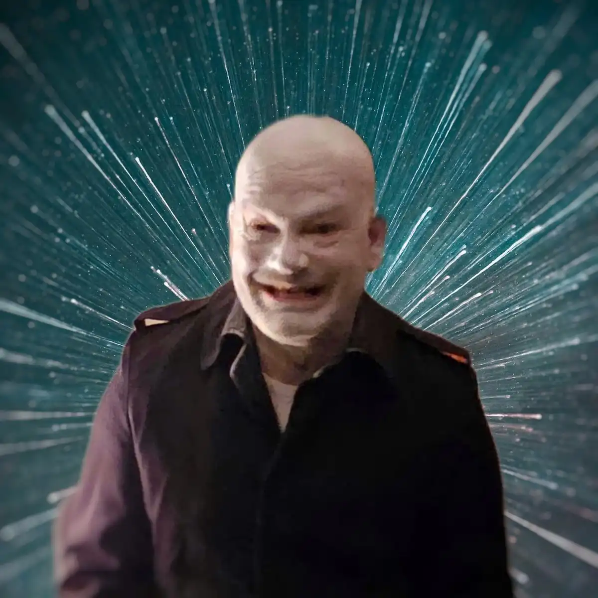 A bald man with a wide, unsettling grin wearing a dark collared shirt is centered against a teal background with white…