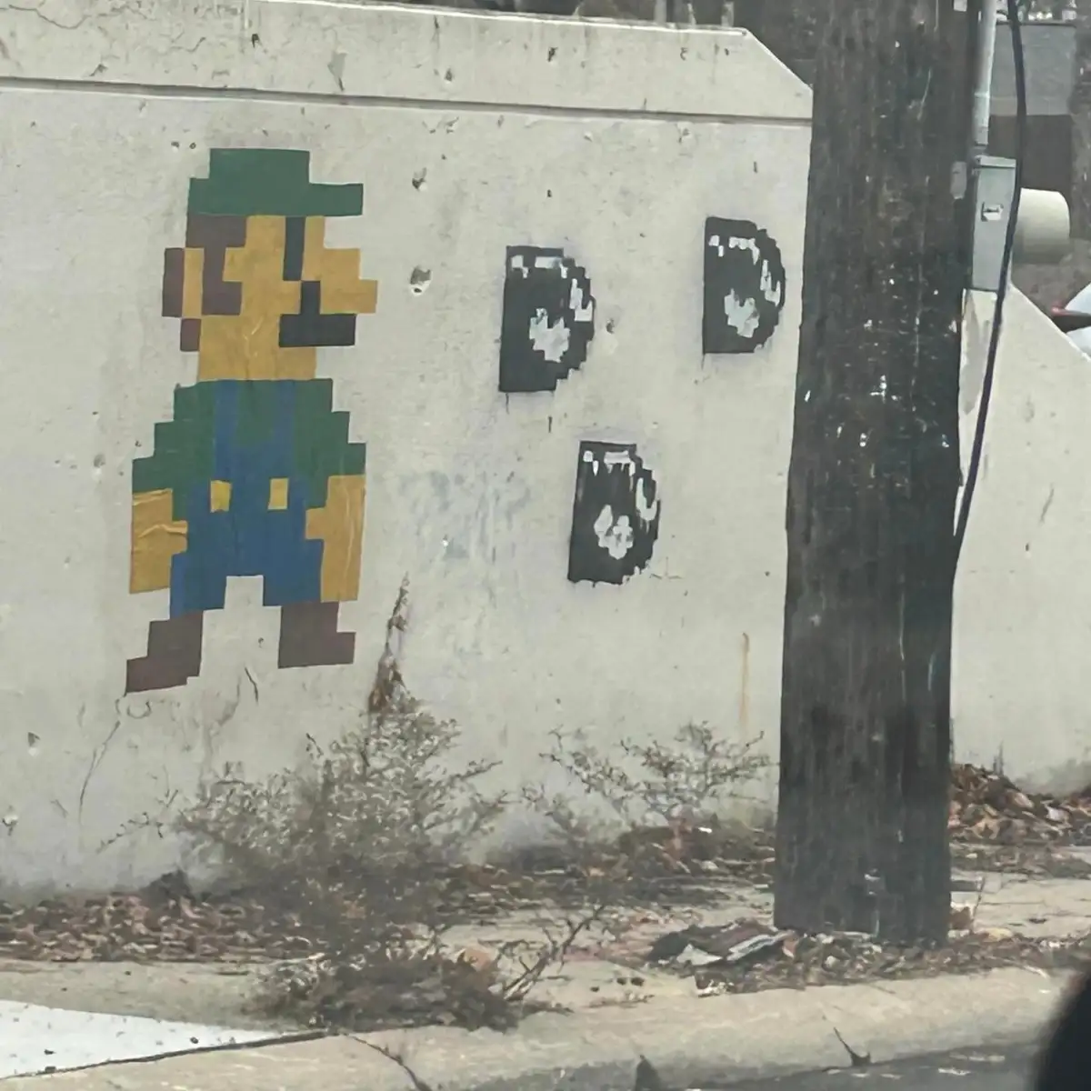 A weathered concrete wall features a pixelated mural of a character resembling Mario from classic video games, standing next…