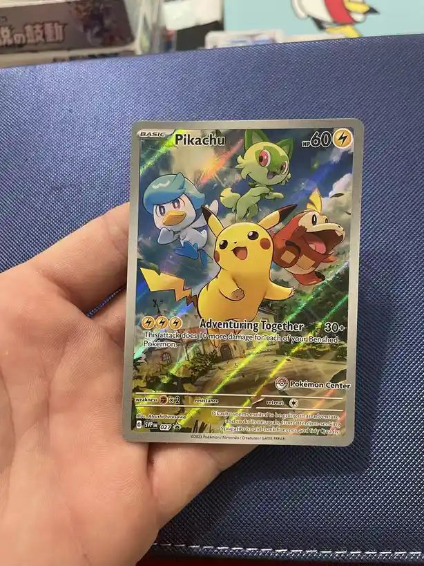 A hand holds a shiny Pokémon TCG card featuring Pikachu with three other Pokémon: Sprigatito, Fuecoco, and Quaxly. The…