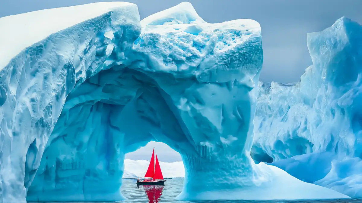 In Ilulissat Icefjord, a glacier meets the ocean, fragmenting into a maze of floating icebergs. A small, red sailboat…