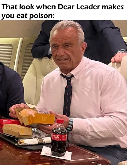 A man in a white shirt and patterned tie sits at a table with a McDonald's meal and a Coca-Cola bottle, holding a partially…
