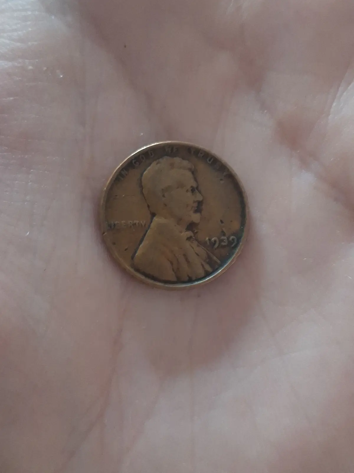 A close-up photo shows a 1939 U.S. Lincoln penny resting in the center of an open palm, with the coin's worn profile and…