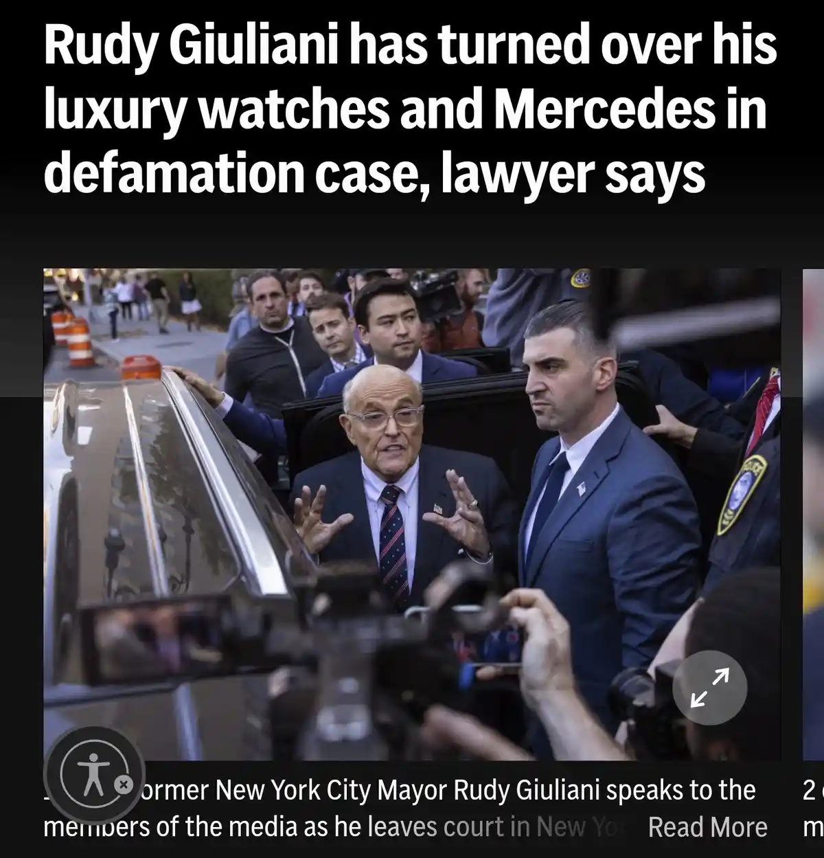 An image of Rudy Giuliani exiting a black Mercedes-Benz car, surrounded by reporters and security, with his hands raised as…