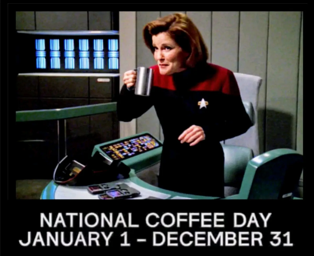 A woman in a red and black Starfleet uniform from Star Trek holds a metal mug while seated at a futuristic console. The…