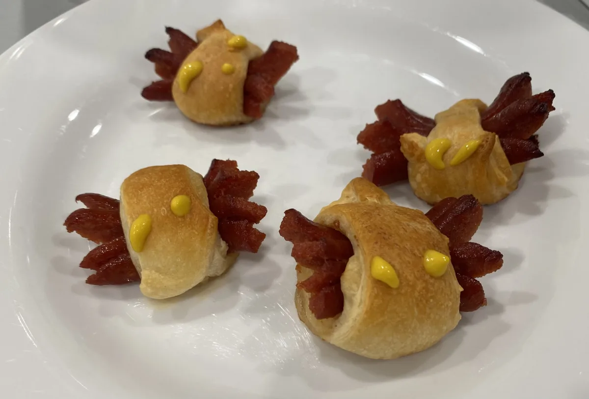 four golden-brown pastry appetizers shaped like small birds, each decorated with yellow mustard dots for eyes and crispy…