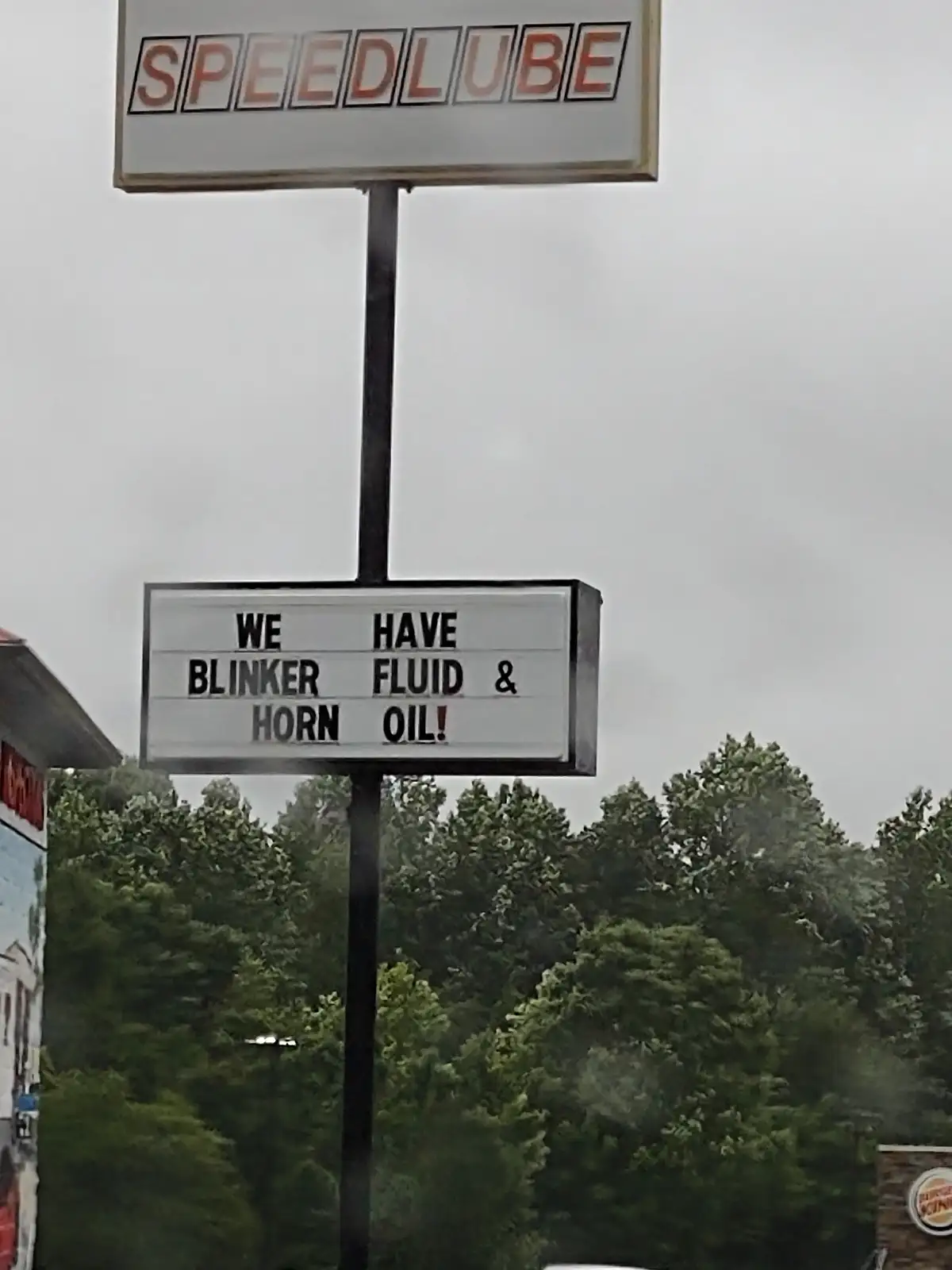 A photo of a Speedlube auto shop sign with a marquee below it that reads 'WE HAVE BLINKER FLUID & HORN OIL!'. The background…