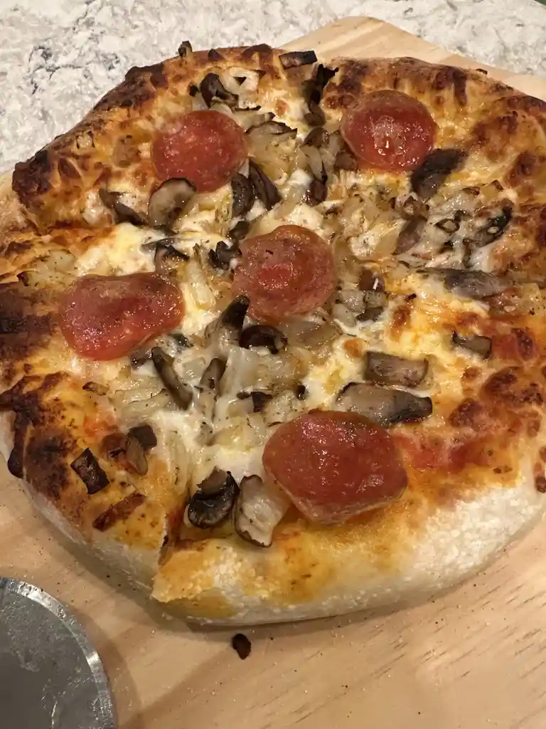 A close-up photo of a freshly baked pizza with pepperoni, mushrooms, and onions on a wooden board, with the overlaid text 'i…