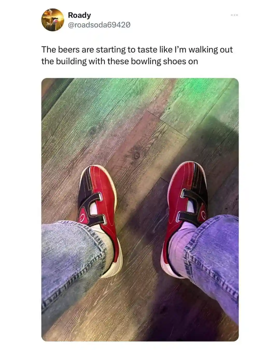 A first-person view of someone wearing red and black bowling shoes with velcro straps, paired with jeans and socks, standing…
