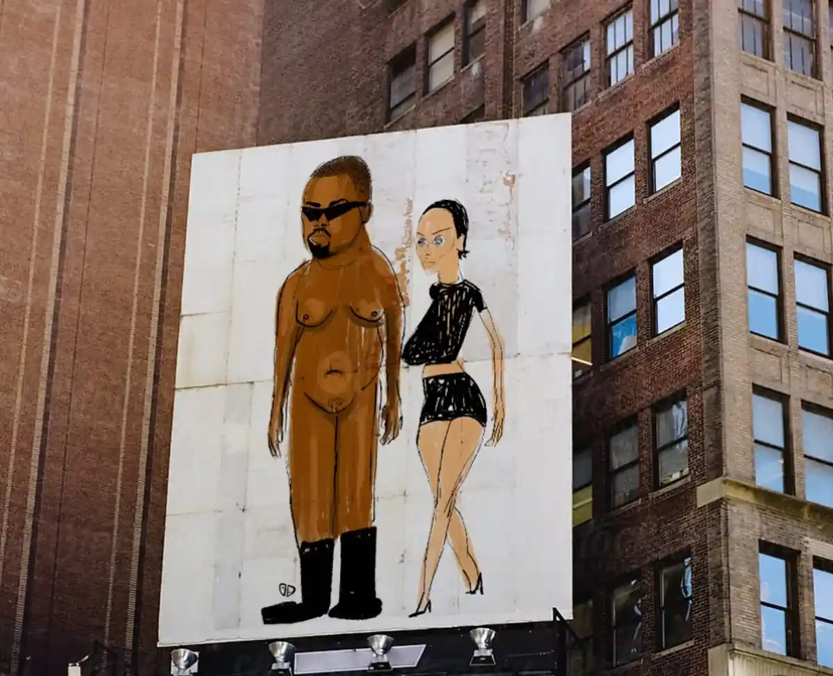 A large outdoor billboard depicts a cartoon-style illustration of Kanye West, shirtless and wearing sunglasses and black…