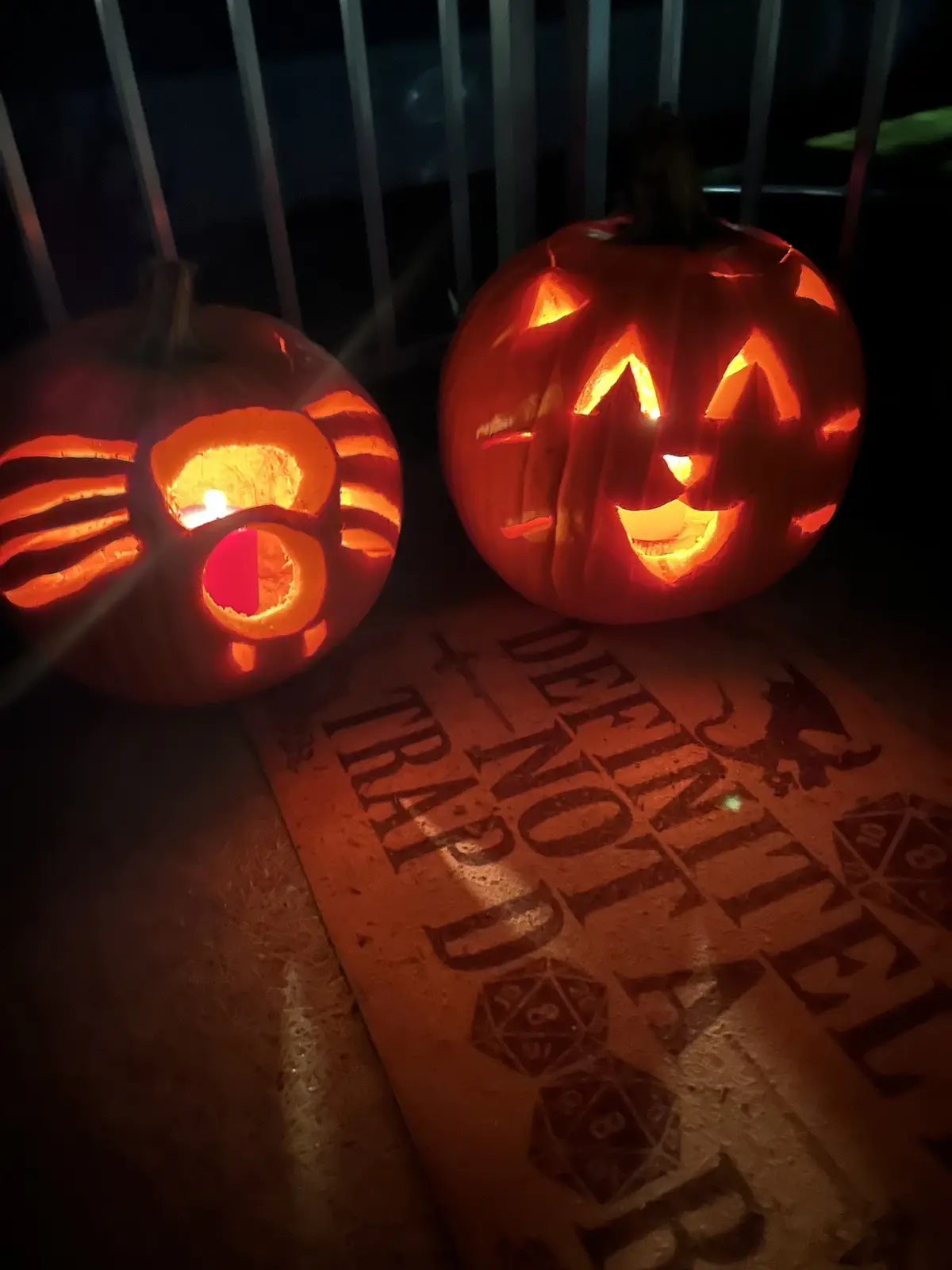 Two carved Halloween pumpkins glow in the dark, one with a classic jack-o'-lantern face and the other with a cat-like design…