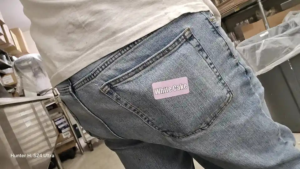 A close-up photo shows the back of a person wearing light blue jeans and a white t-shirt, with a pink rectangular sticker…