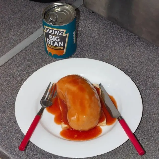 A white plate holds a large, rounded, brownish food item covered in red sauce, flanked by a fork and knife with red handles…