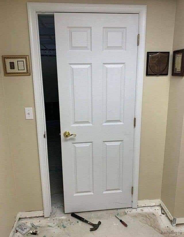 A white six-panel interior door is ajar, revealing a dark room behind it. The floor in front of the door is covered in…