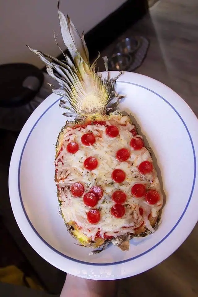 A whole pineapple, with its crown intact, is hollowed out and filled with melted cheese, tomato sauce, and pepperoni slices…
