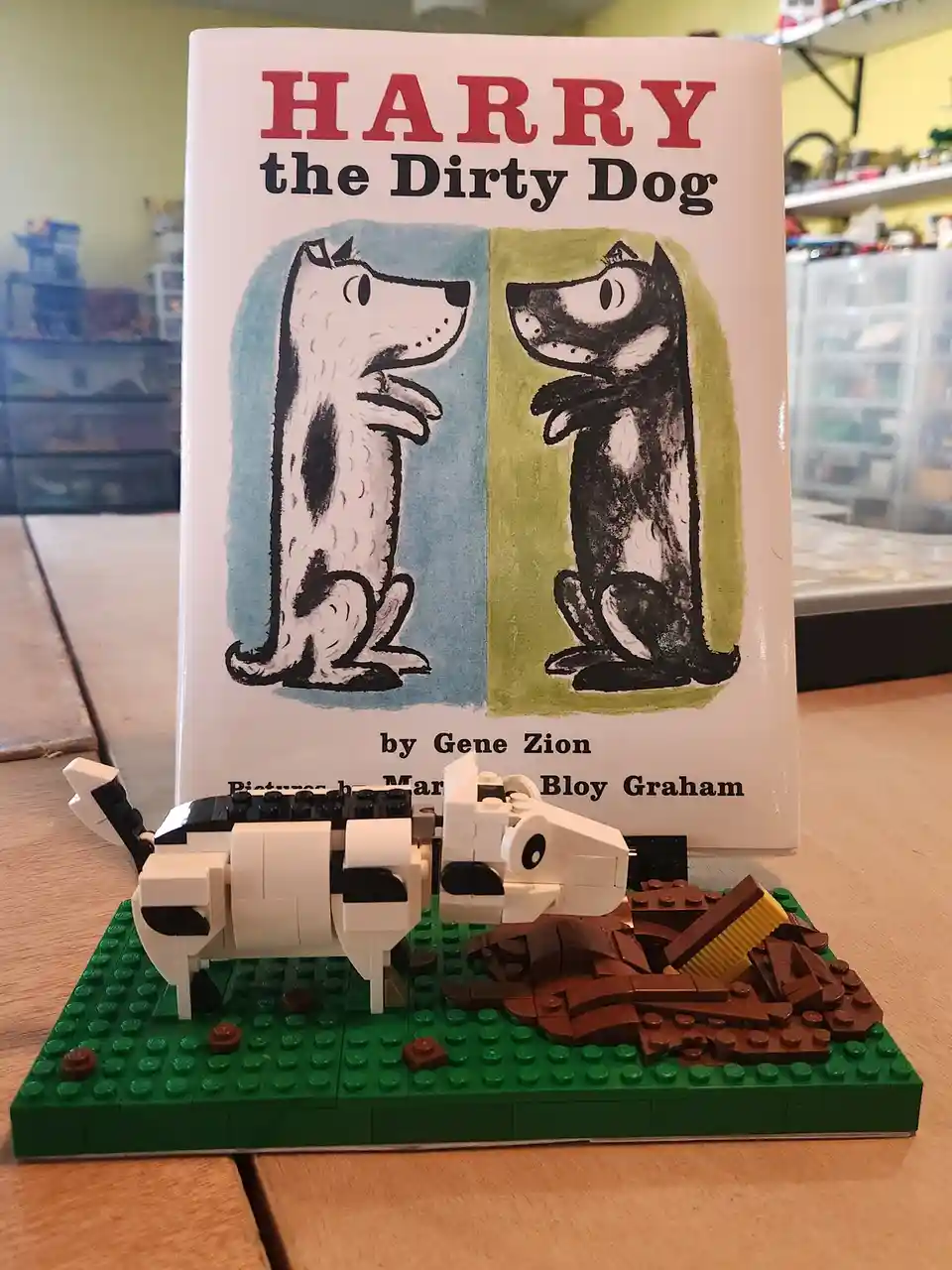 A child's book titled 'Harry the Dirty Dog' by Gene Zion stands upright behind a LEGO diorama. The diorama features a white…
