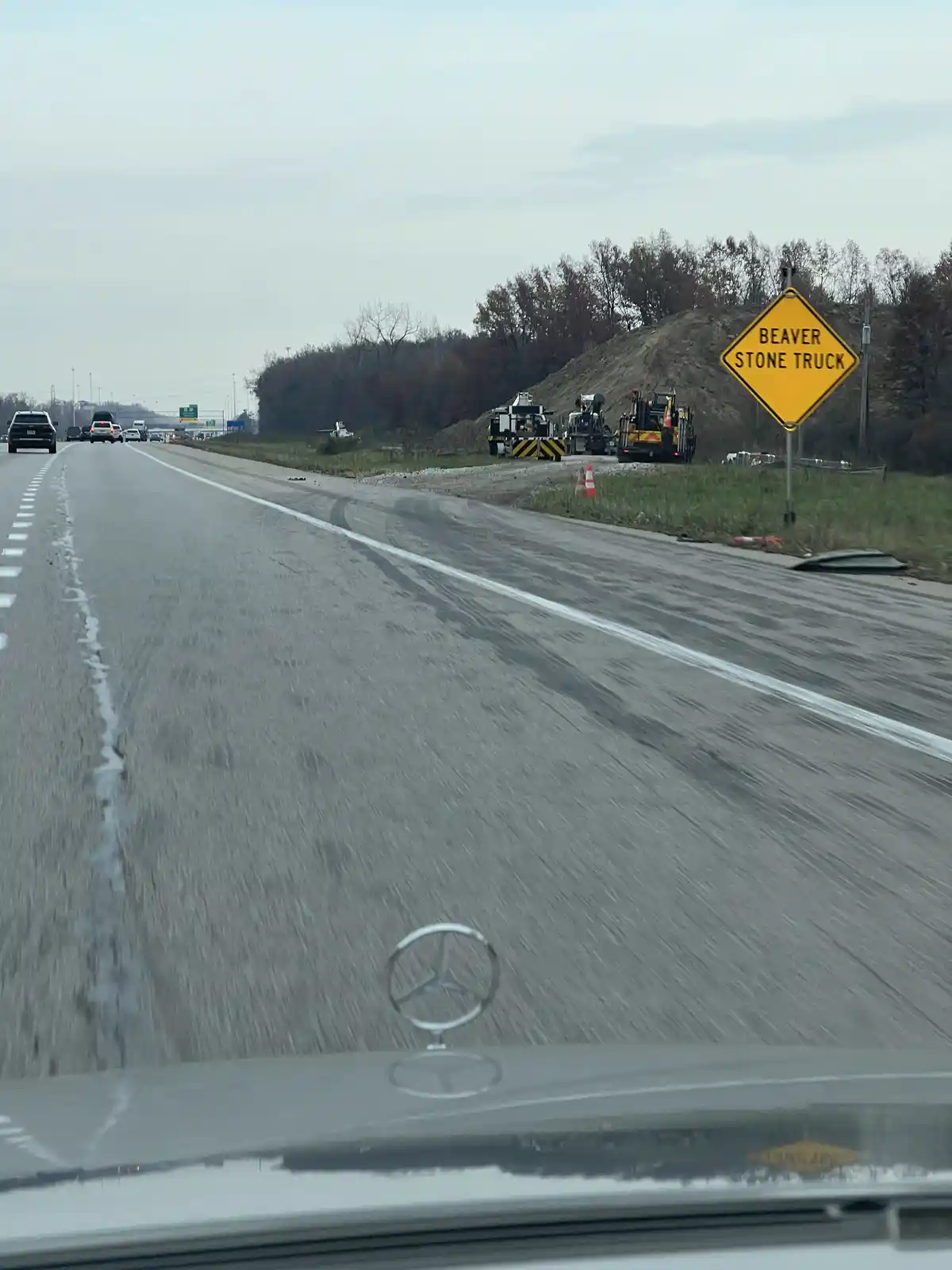 A photo taken from inside a car shows a yellow diamond-shaped road sign that reads 'BEAVER STONE TRUCK' next to construction…