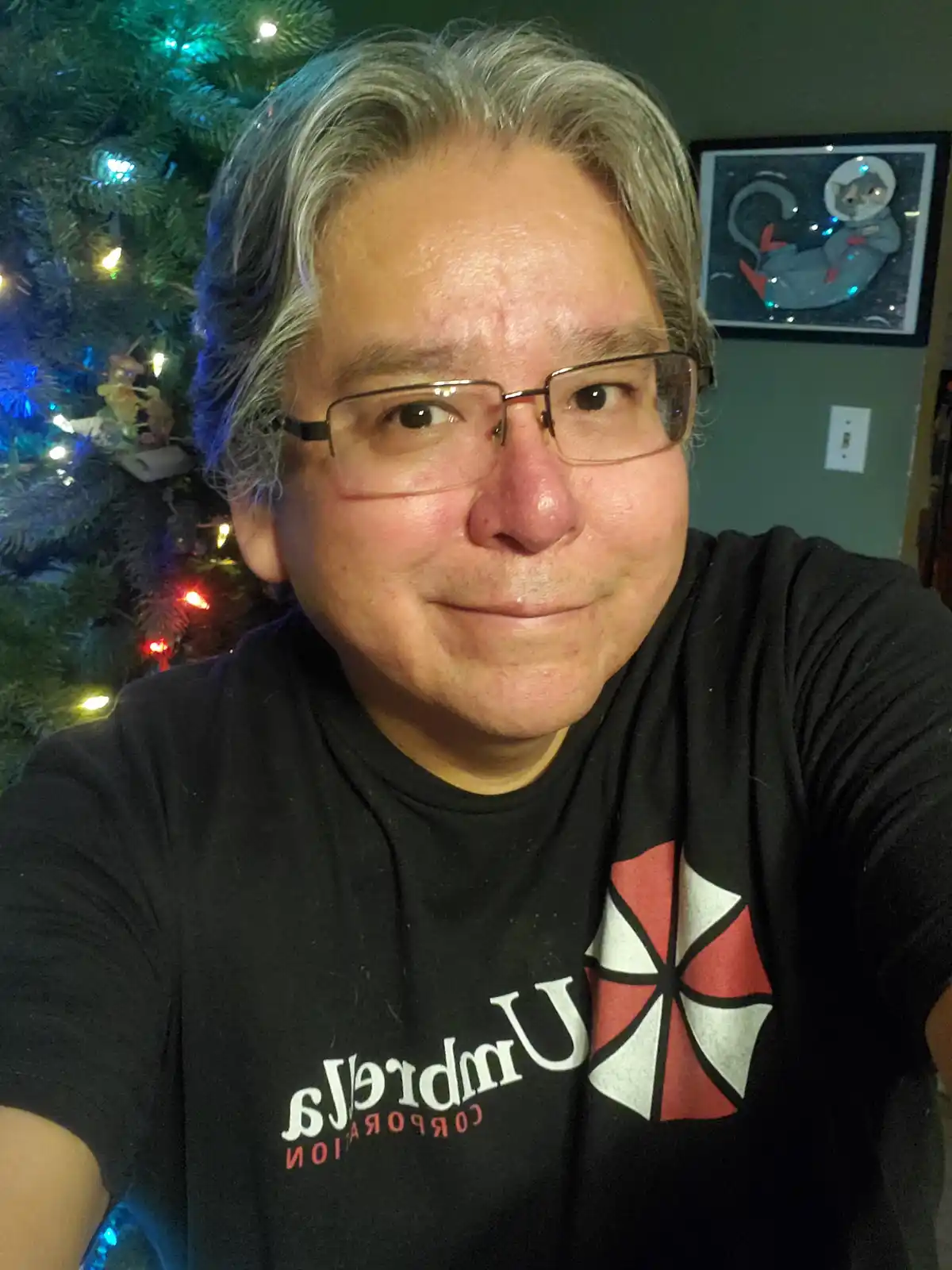 A man with gray hair and glasses wears a black t-shirt with the 'Umbrella Corporation' logo from Resident Evil, but the text…