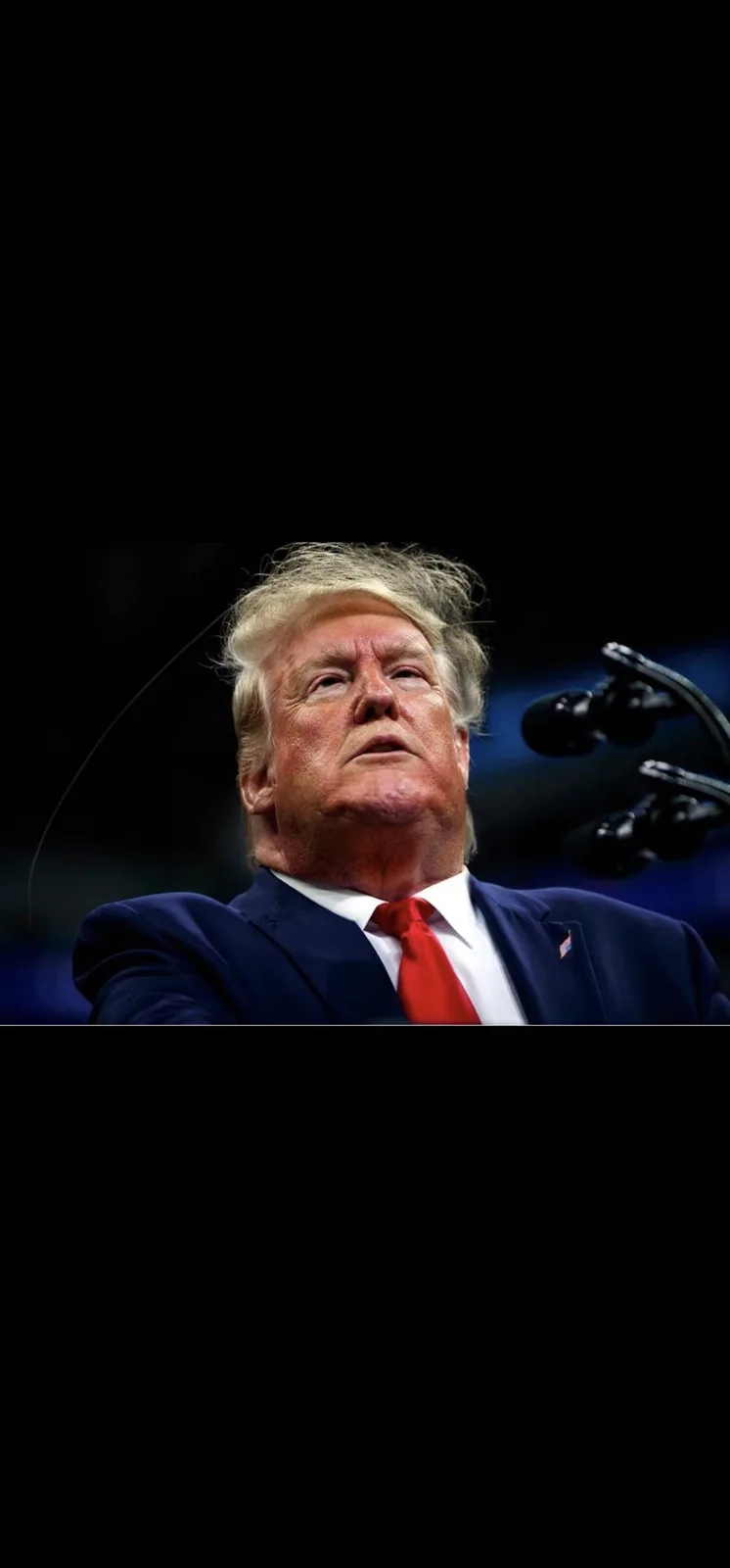 A close-up photo of Donald Trump looking upward with a serious expression, wearing a dark suit, white shirt, and red tie…