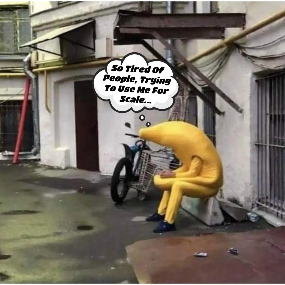 A person in a full-body yellow banana costume sits slumped on a concrete block in an alleyway, looking exhausted. A thought…
