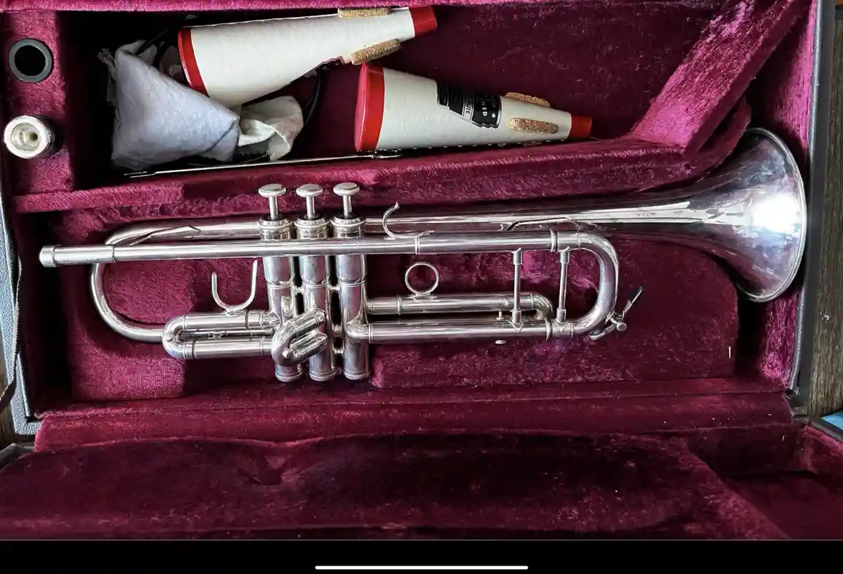 A silver trumpet rests in a burgundy velvet case, with its mouthpieces and cleaning cloth stored in the upper compartment…
