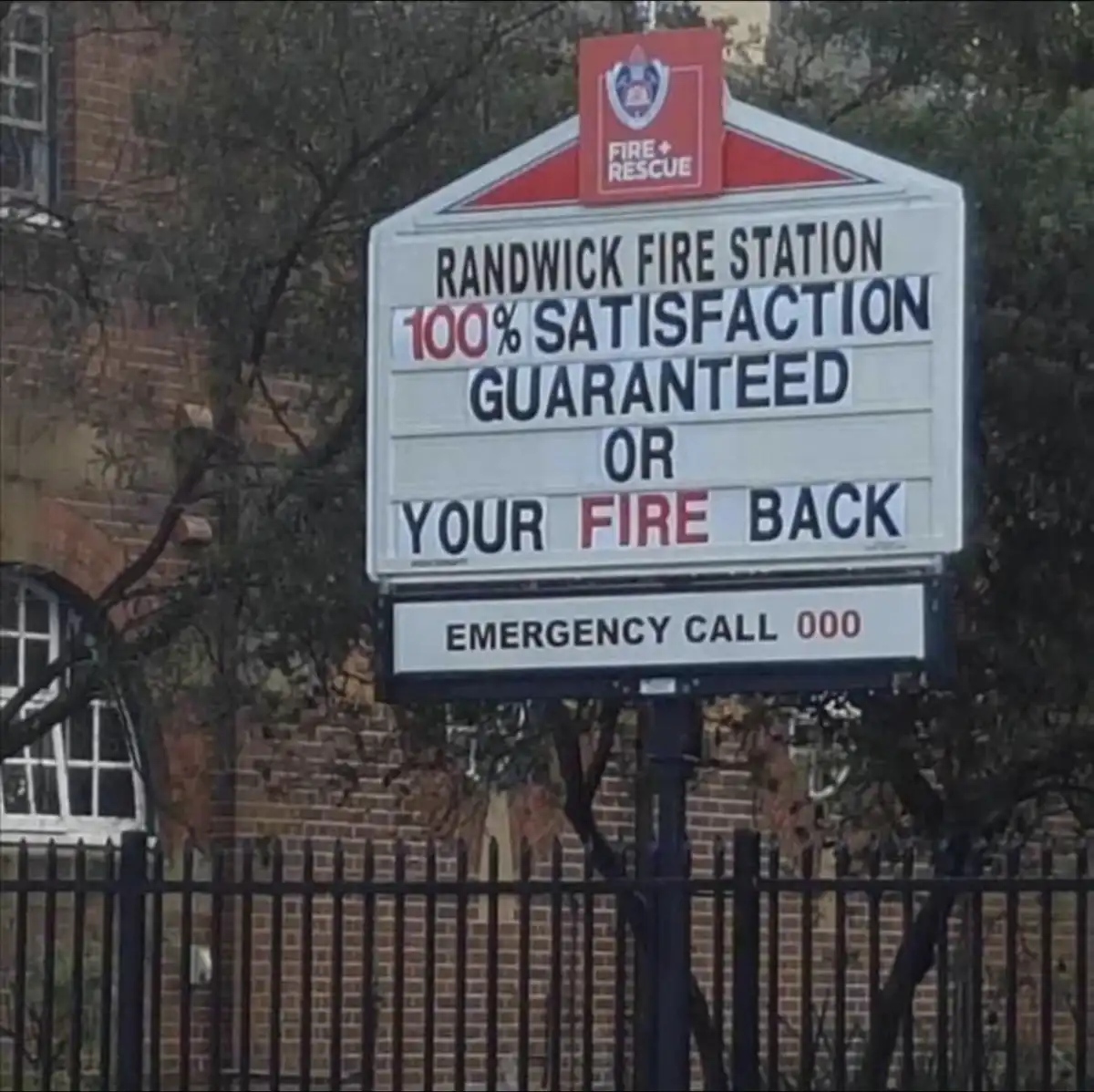 A sign for Randwick Fire Station displays a humorous customer satisfaction guarantee: '100% SATISFACTION GUARANTEED OR YOUR…