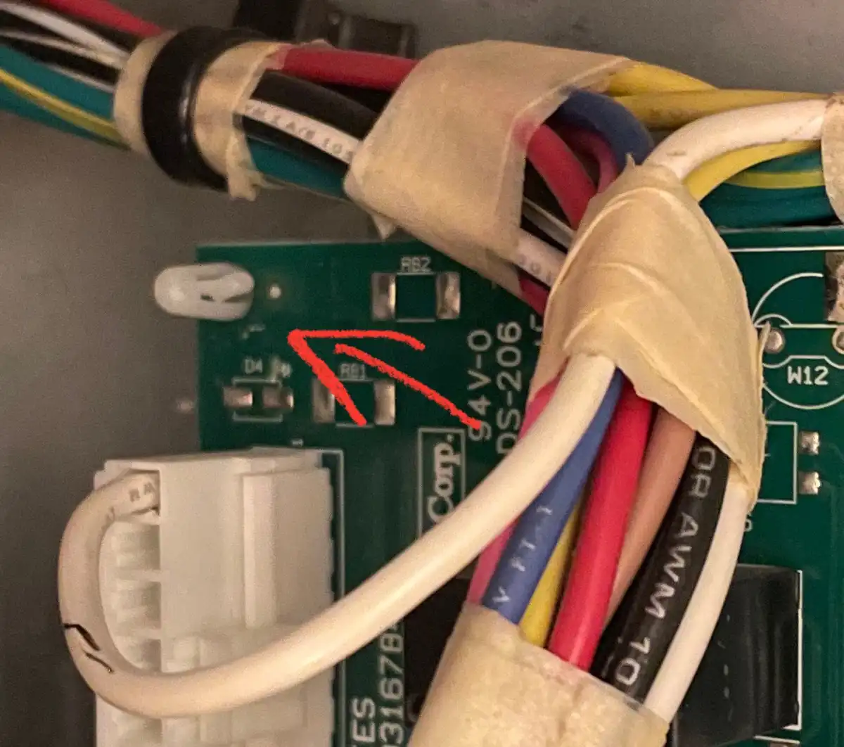 A close-up photo of a green circuit board with various electronic components and bundled wires held together with beige…
