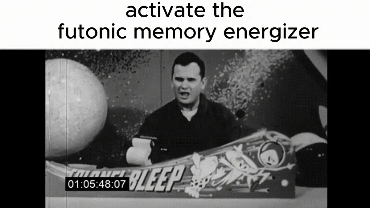 A black-and-white image shows a man in a dark shirt sitting at a desk with a large, decorated box labeled 'FUTONIC BLEEP' in…