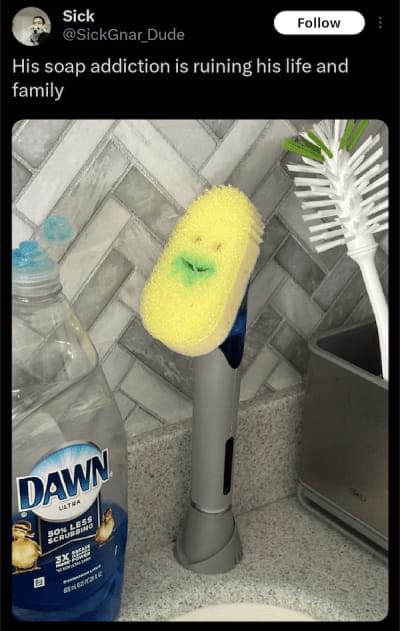 A yellow sponge with a crudely drawn smiling face and green soap residue on its mouth is mounted on a gray electric…