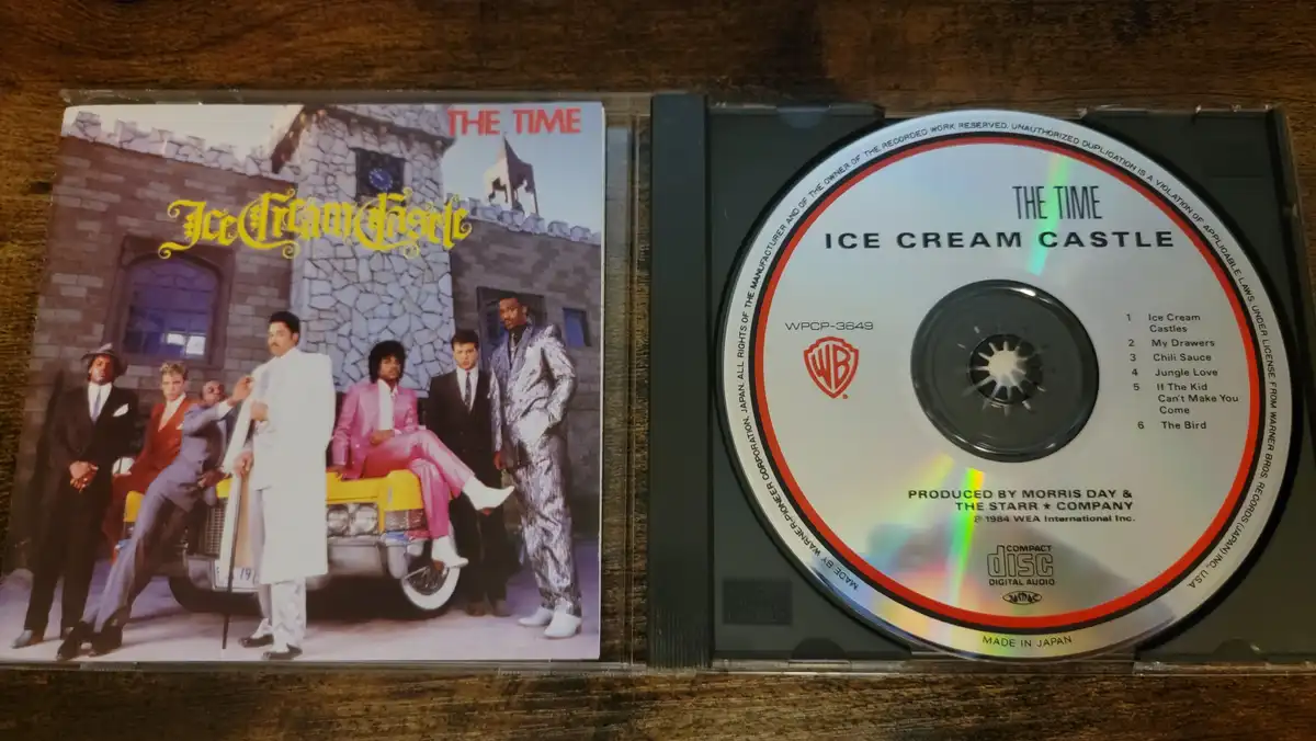 A physical CD case for The Time's 1984 album 'Ice Cream Castle' is open, showing the album cover with the band posing in…